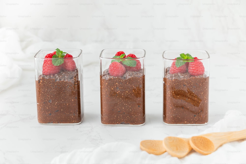 three glasses of chocolate pudding with raspberries on top