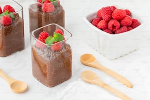 raspberries and chocolate pudding in glass containers with wooden spoons