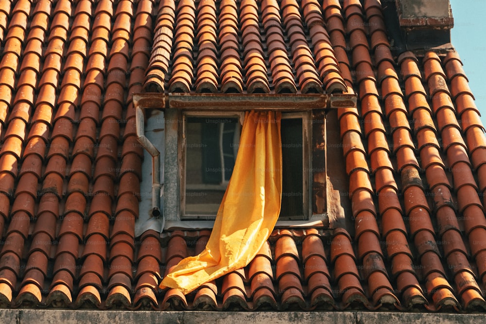 una ventana con una cortina amarilla en un techo de tejas rojas