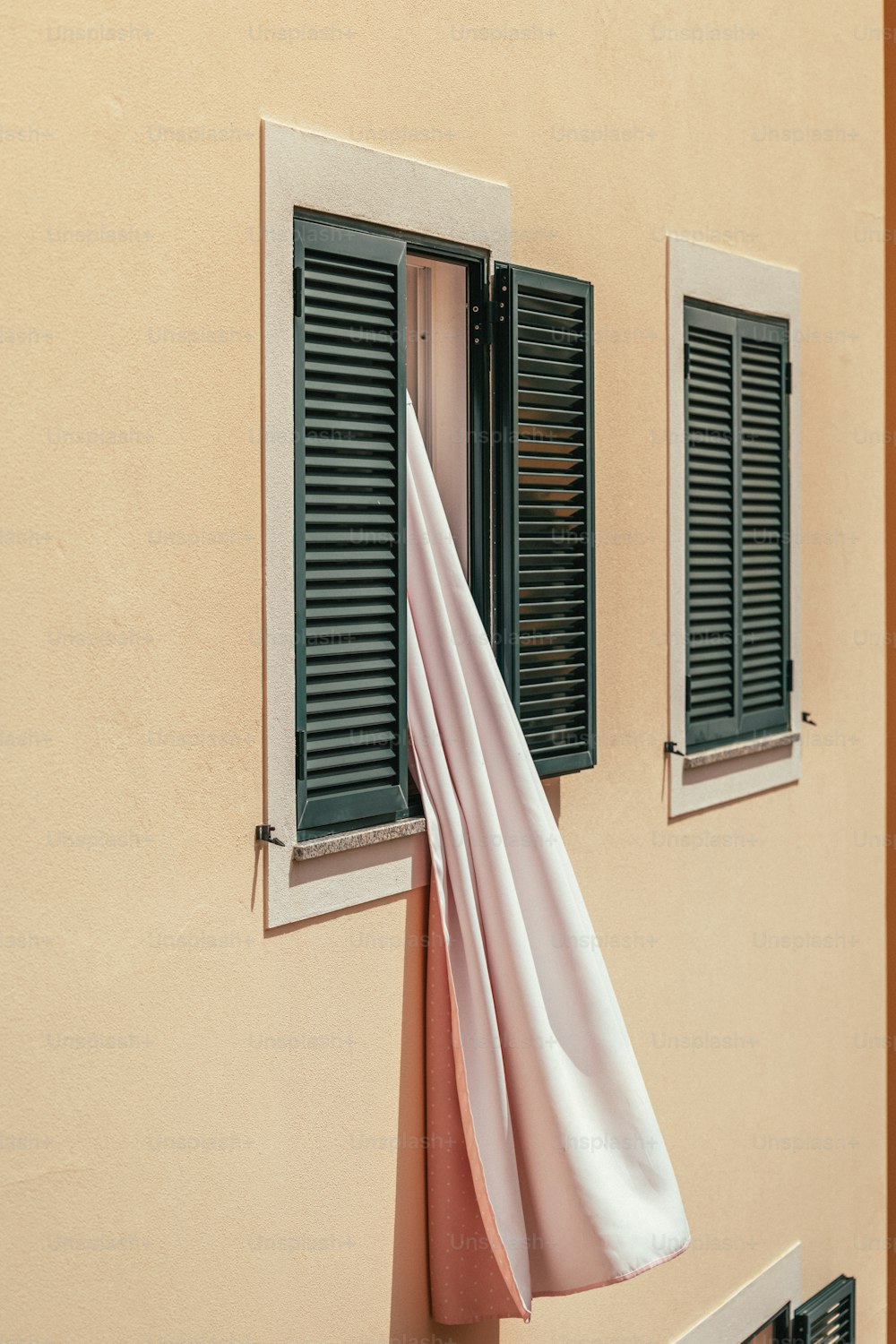 ein rosa Handtuch, das an einem Fenster mit zwei schwarzen Fensterläden hängt