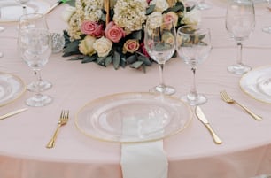 a table set for a formal dinner with pink and white flowers