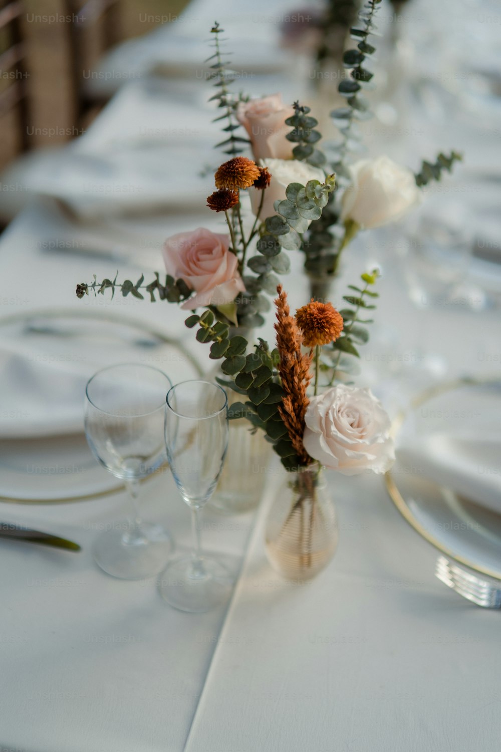 uma mesa com um vaso de flores e taças de vinho
