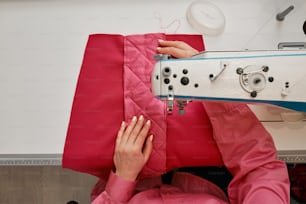 a woman is sewing on a pink quilt