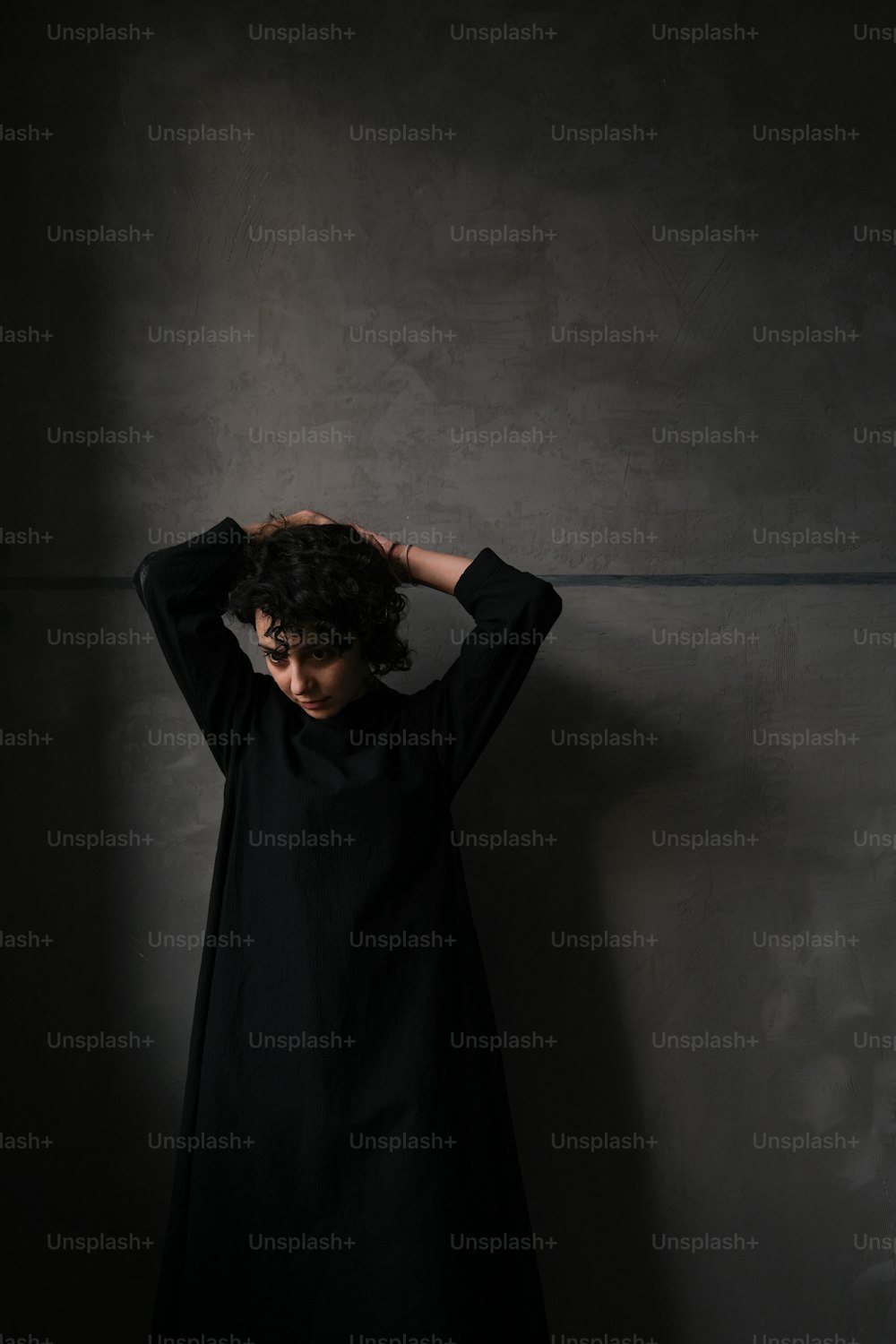 Una mujer parada en una habitación oscura con las manos en la cabeza