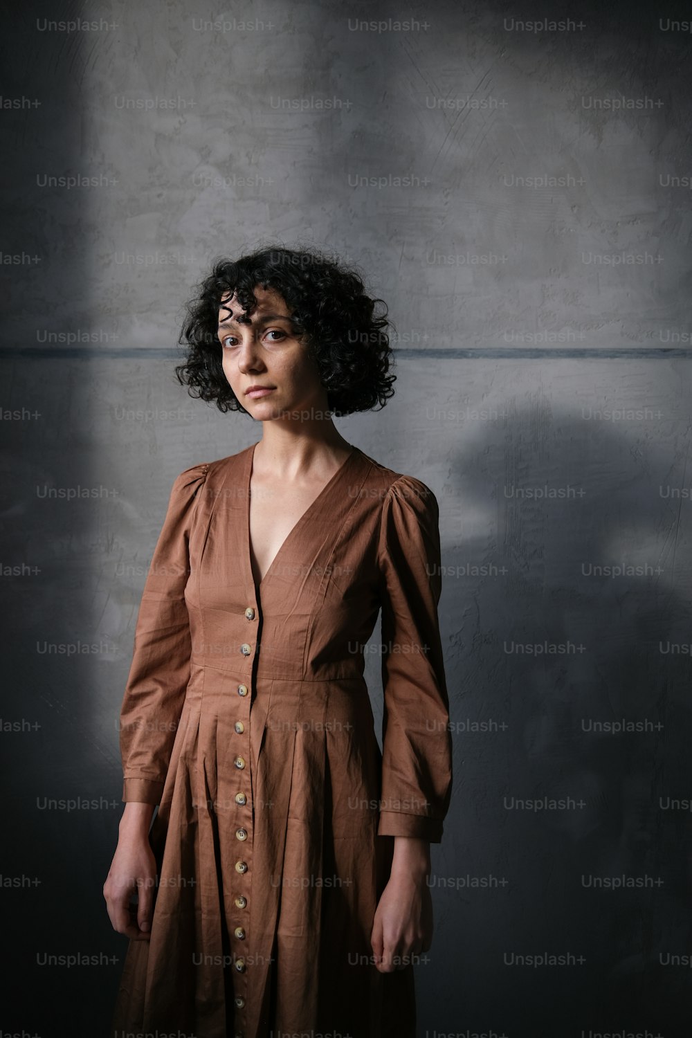 Una mujer con un vestido marrón parada en una habitación oscura