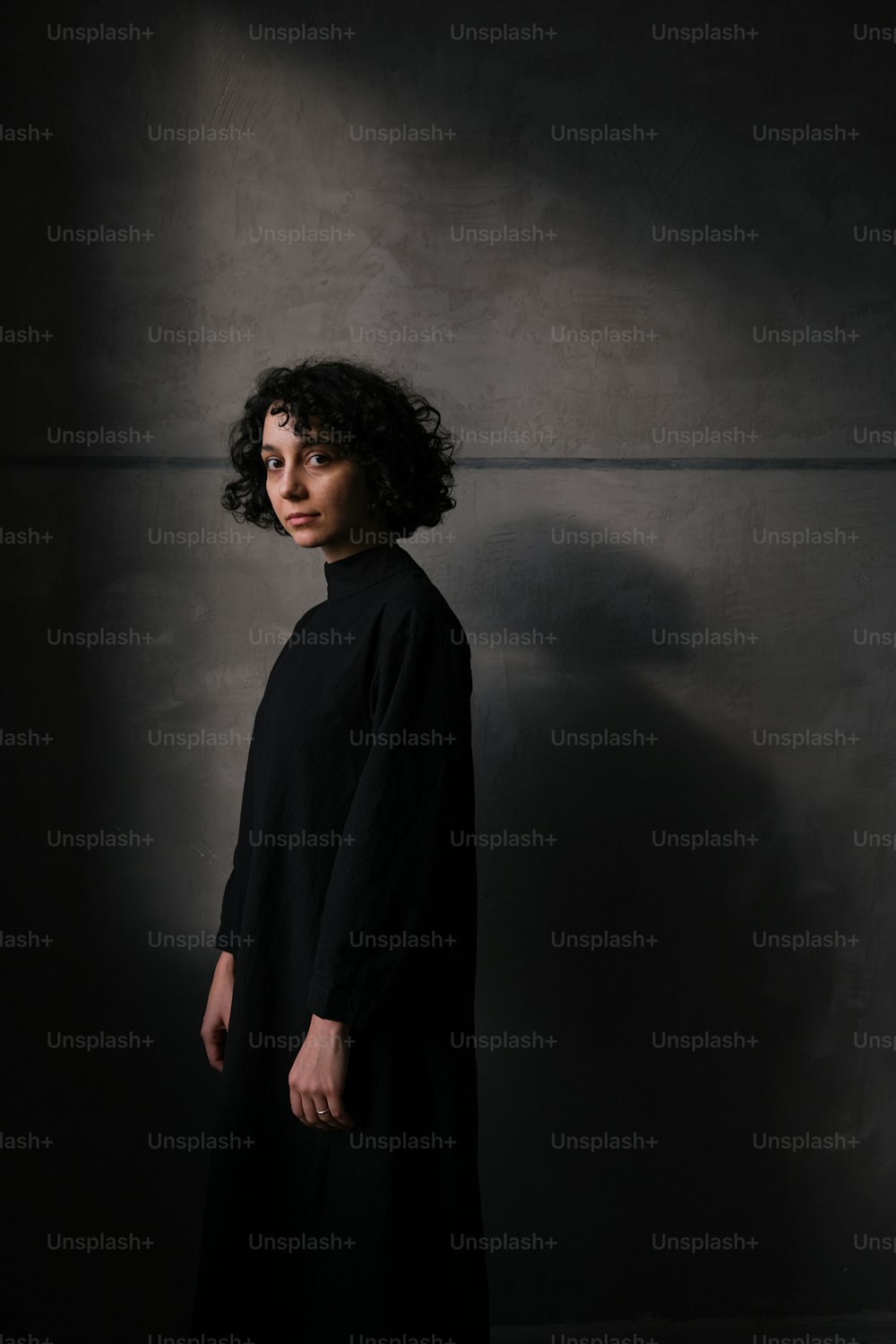 Une femme debout dans une pièce sombre vêtue d’une robe noire