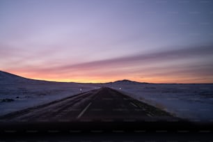 the sun is setting on a snowy road