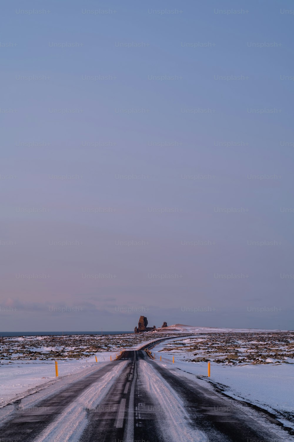 a road with snow on the ground and a large rock in the distance