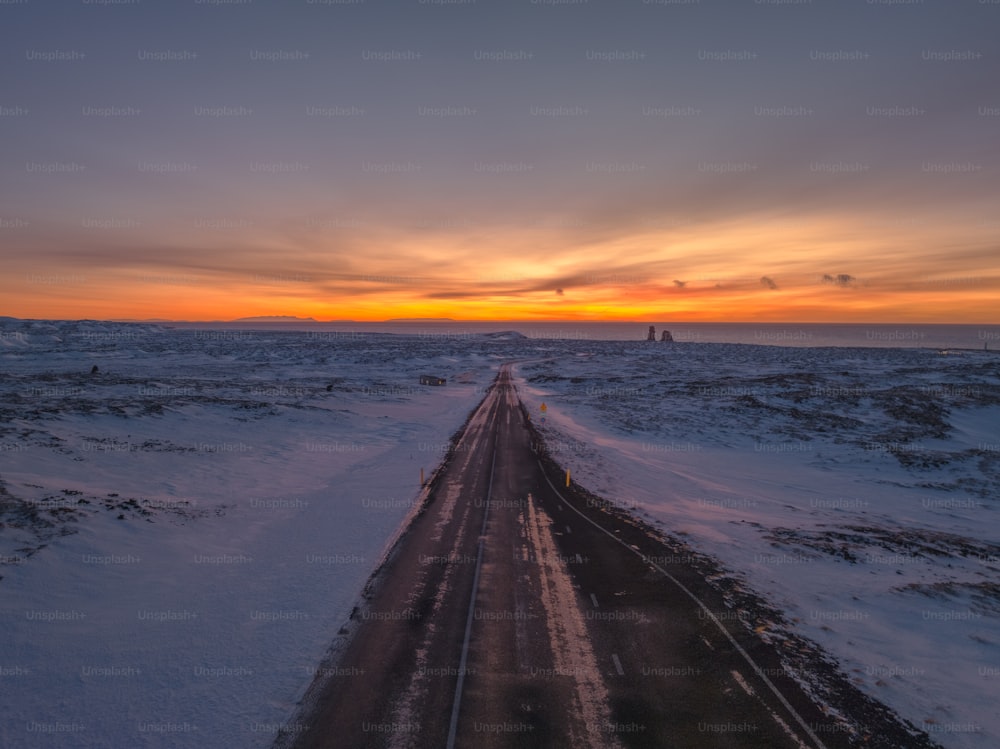 the sun is setting over a snowy road