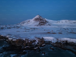 a mountain covered in snow next to a body of water