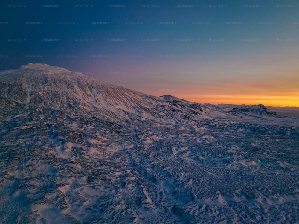 Una montagna coperta di neve con un tramonto sullo sfondo