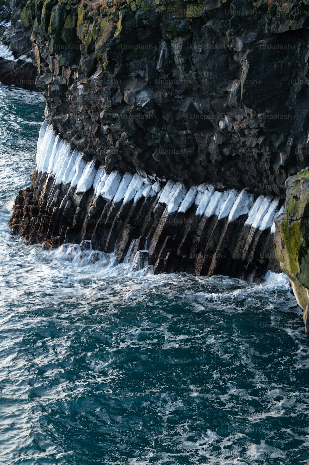 a large rock sticking out of the ocean next to a cliff