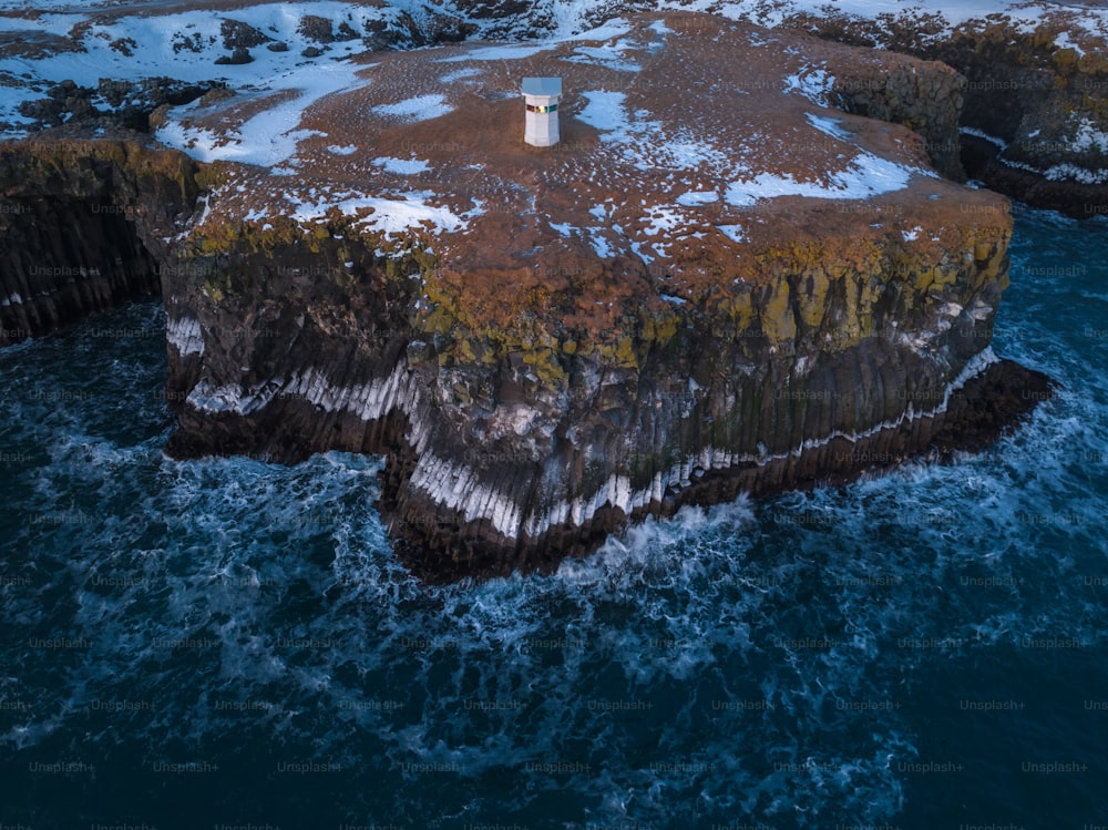 an aerial view of a lighthouse on a rock outcropping in the ocean