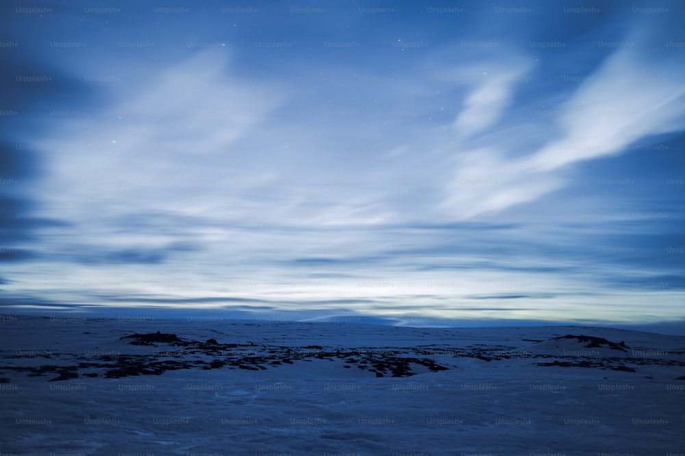 a snow covered field with a sky full of clouds