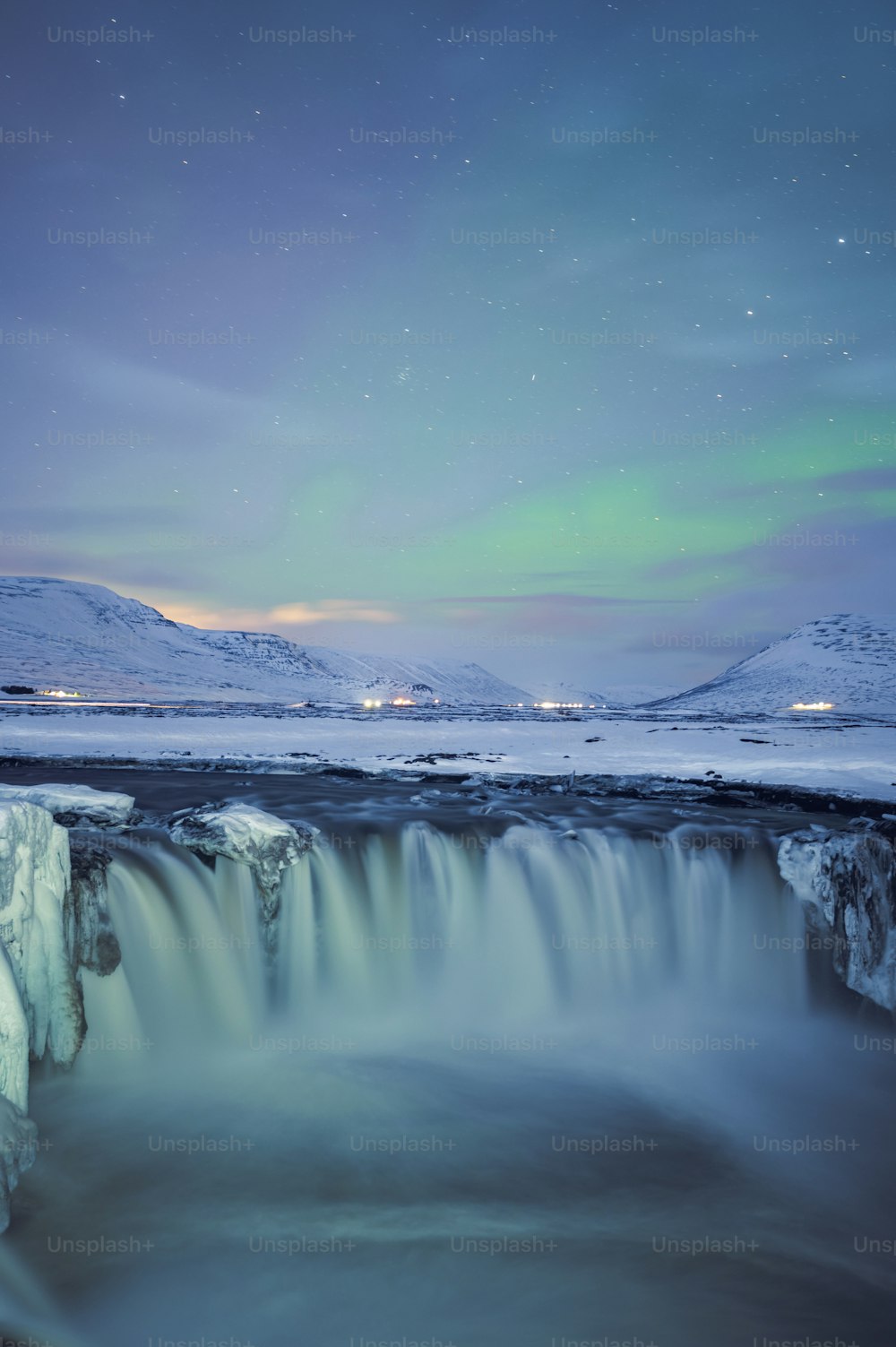Una cascata ghiacciata con una luce verde aurora nel cielo