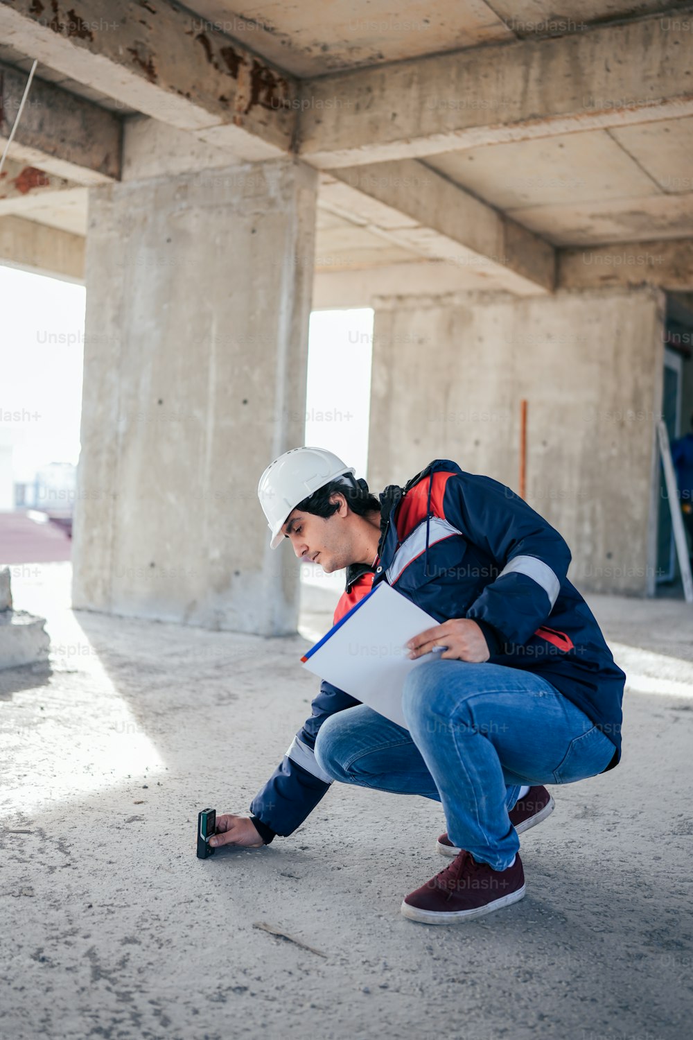 a man in a hard hat and jacket crouching down holding a piece of paper