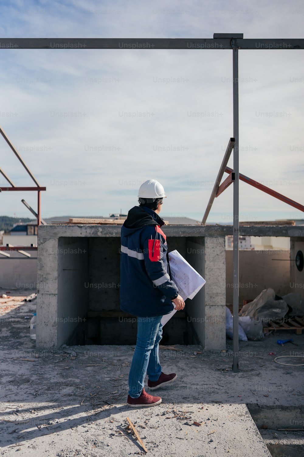 a man in a hard hat and jacket standing in front of a building under construction