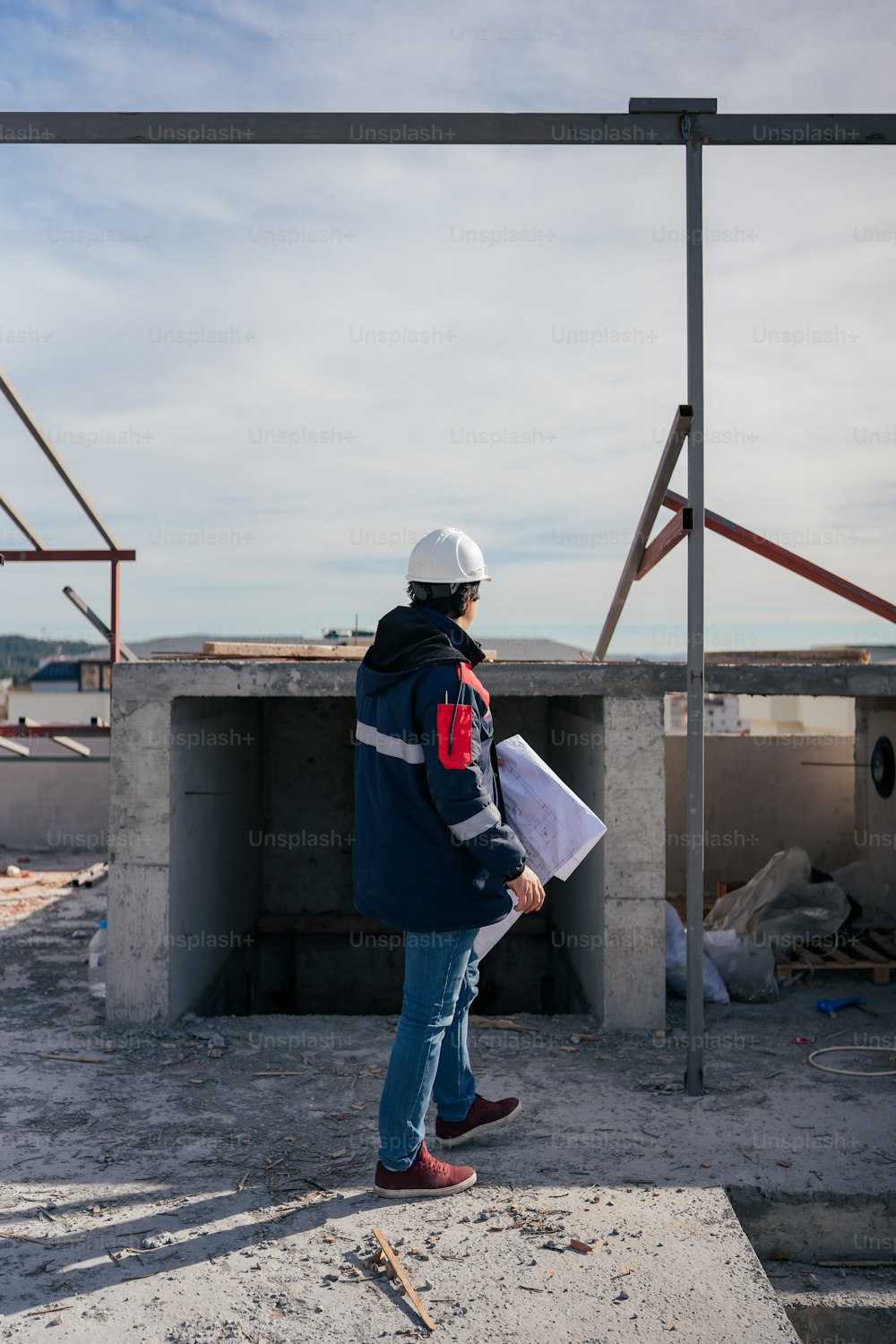 um homem de capacete e jaqueta em pé na frente de um prédio em construção