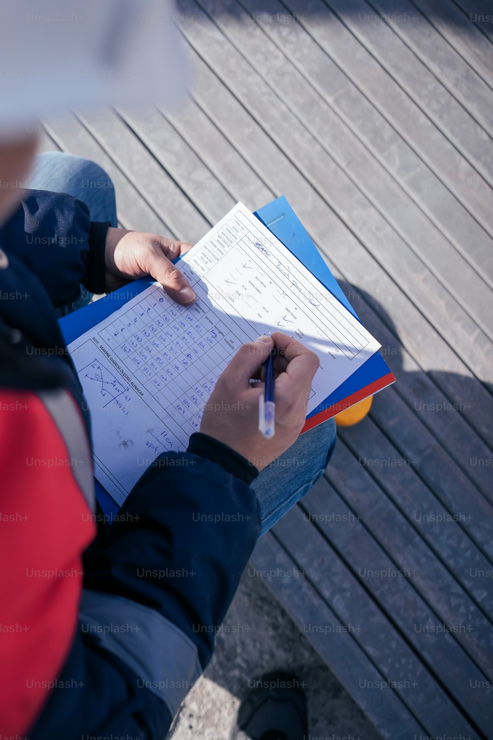 uma pessoa sentada em um banco escrevendo em um pedaço de papel