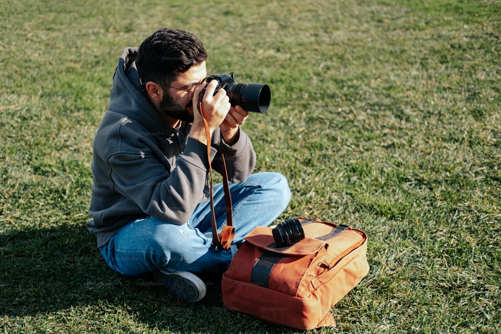 um homem sentado na grama tirando uma foto com uma câmera