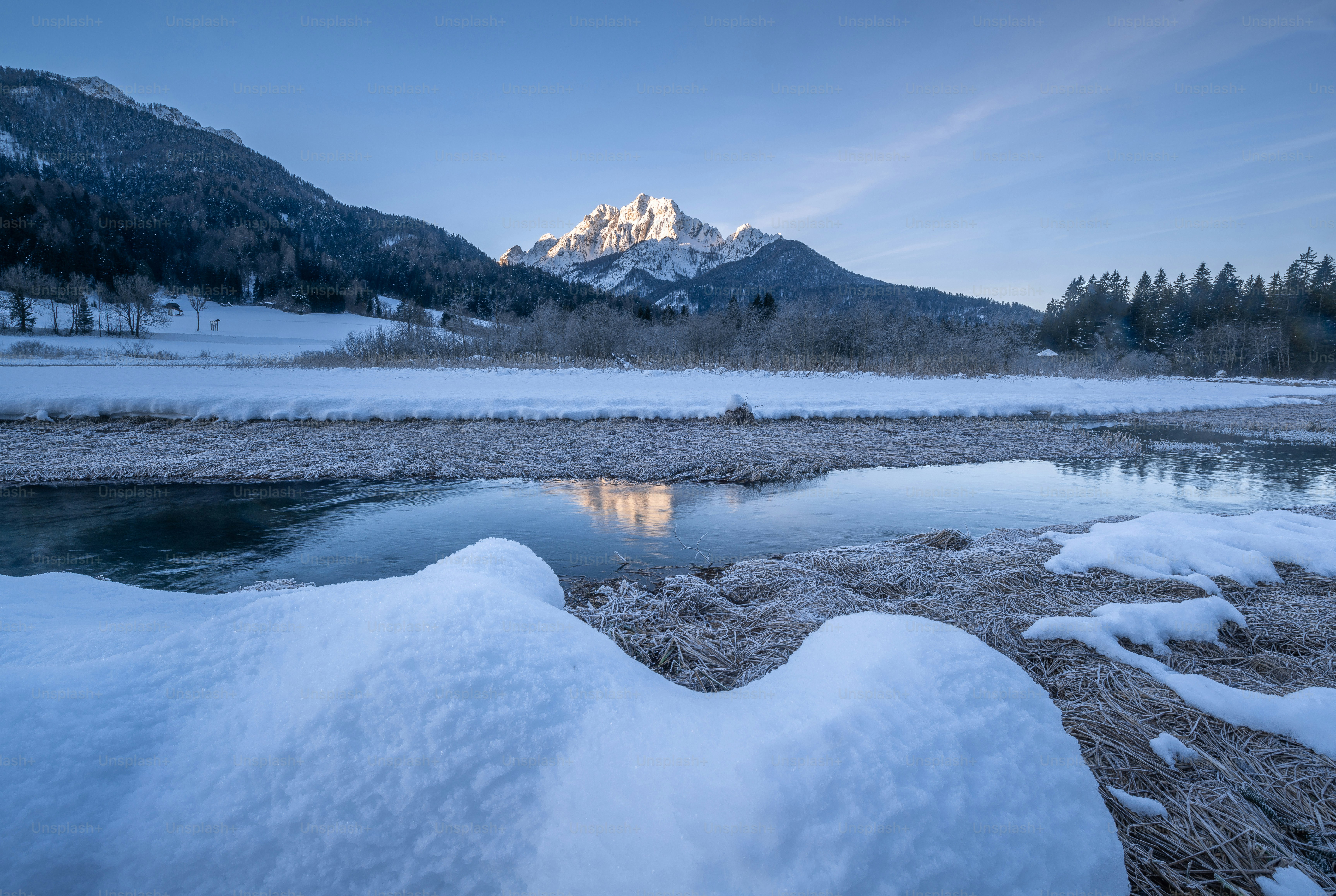 a river with snow on the ground and mountains in the background