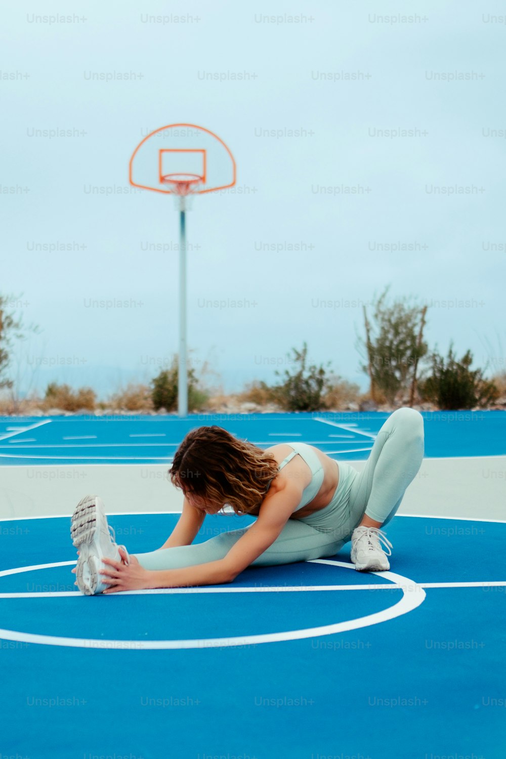 Una mujer sentada en una cancha de baloncesto sosteniendo una botella de agua