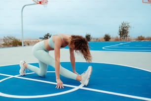 スポーツブラとレギンスを着た女性がバスケットボールコートにうずくまる
