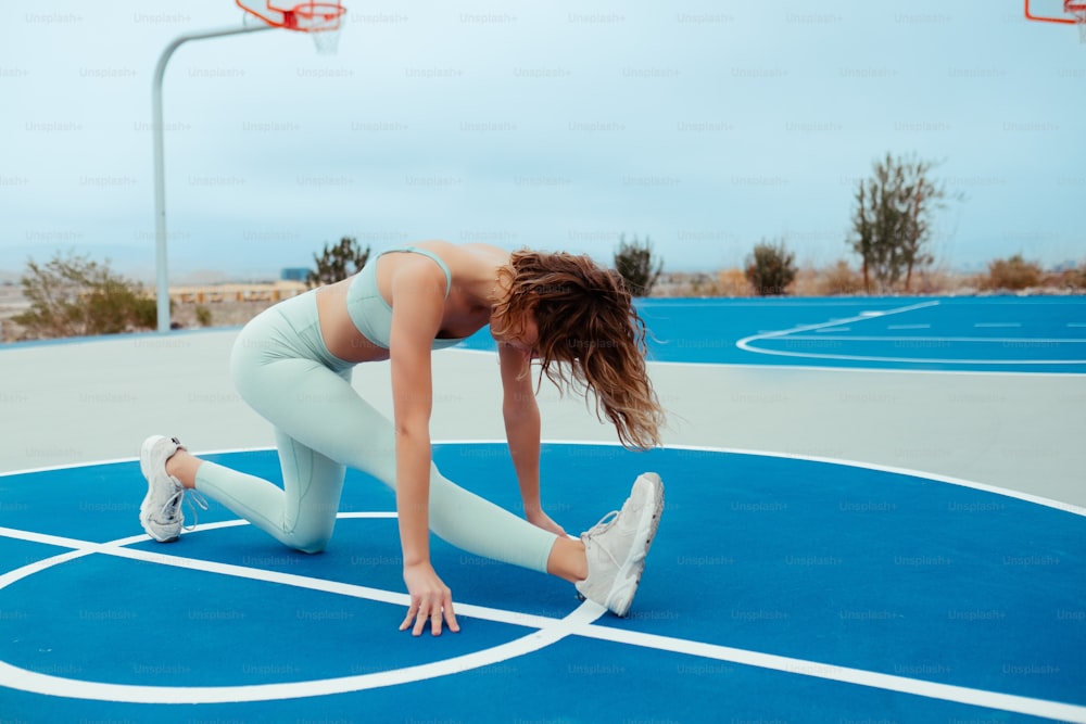 a woman in a sports bra and leggings crouches on a basketball court
