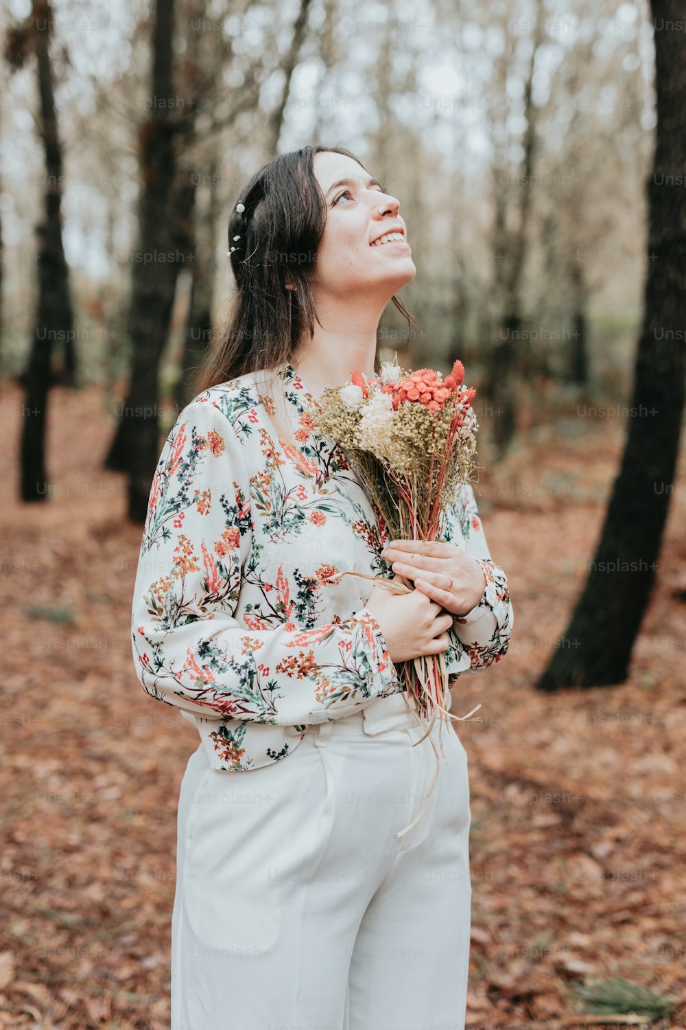 Una donna in piedi in una foresta con in mano un mazzo di fiori