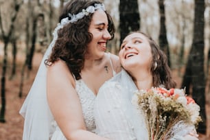 two brides hugging each other in the woods