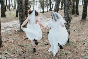 Zwei Bräute laufen Händchen haltend durch den Wald