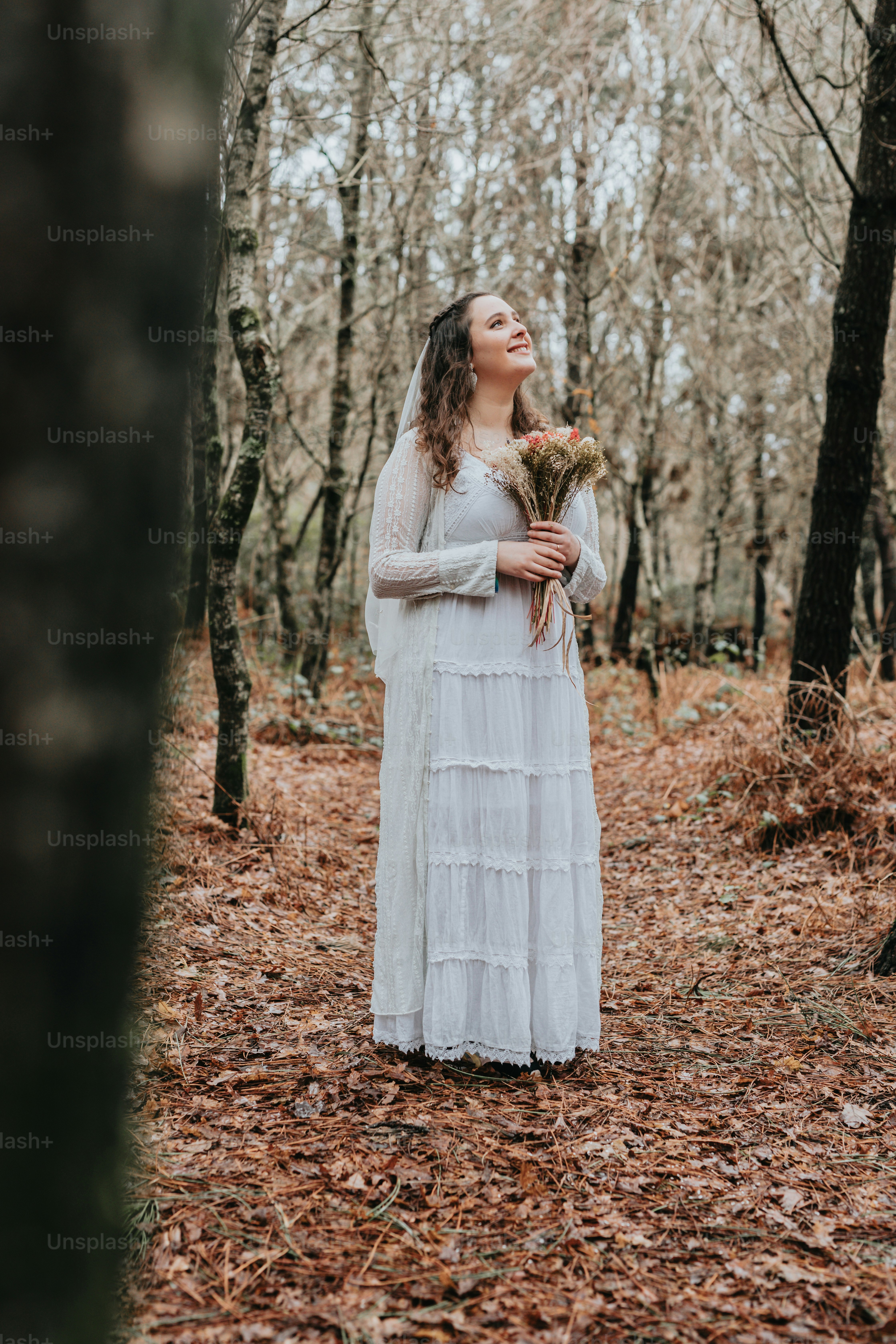 A woman in a white dress standing in a forest photo – Bridal bouquet ...