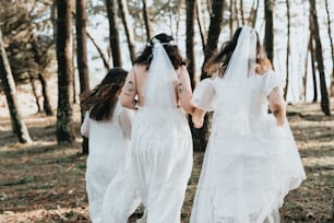 three women in white dresses walking through a forest