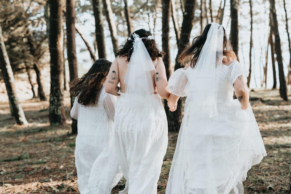 Drei Frauen in weißen Kleidern spazieren durch einen Wald