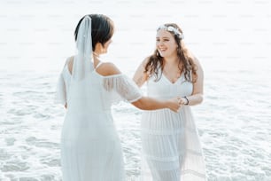 two women in white dresses standing on a beach