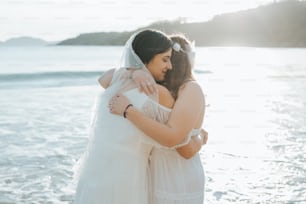 two brides hugging each other on the beach