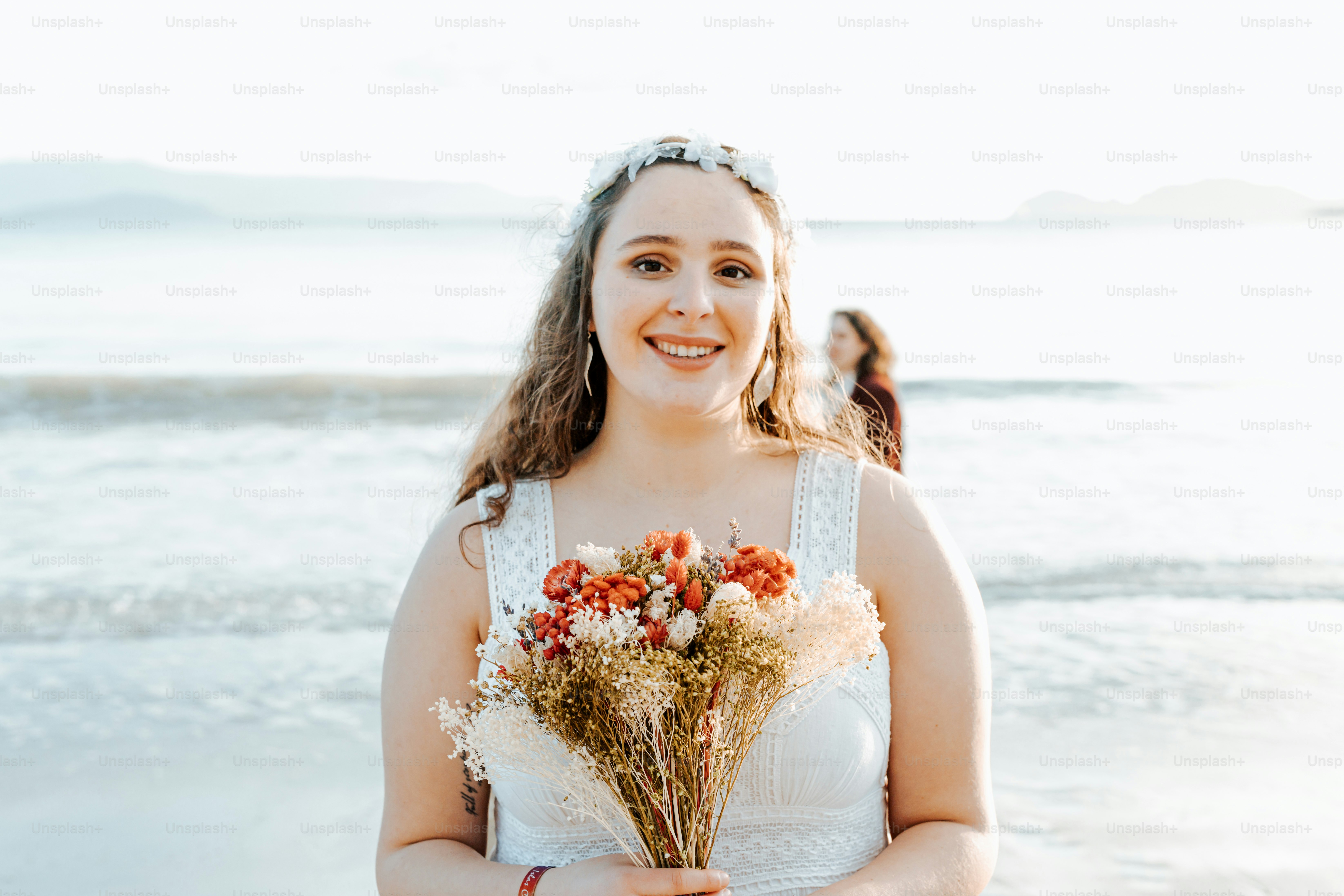 a woman standing on a beach holding a bouquet of flowers