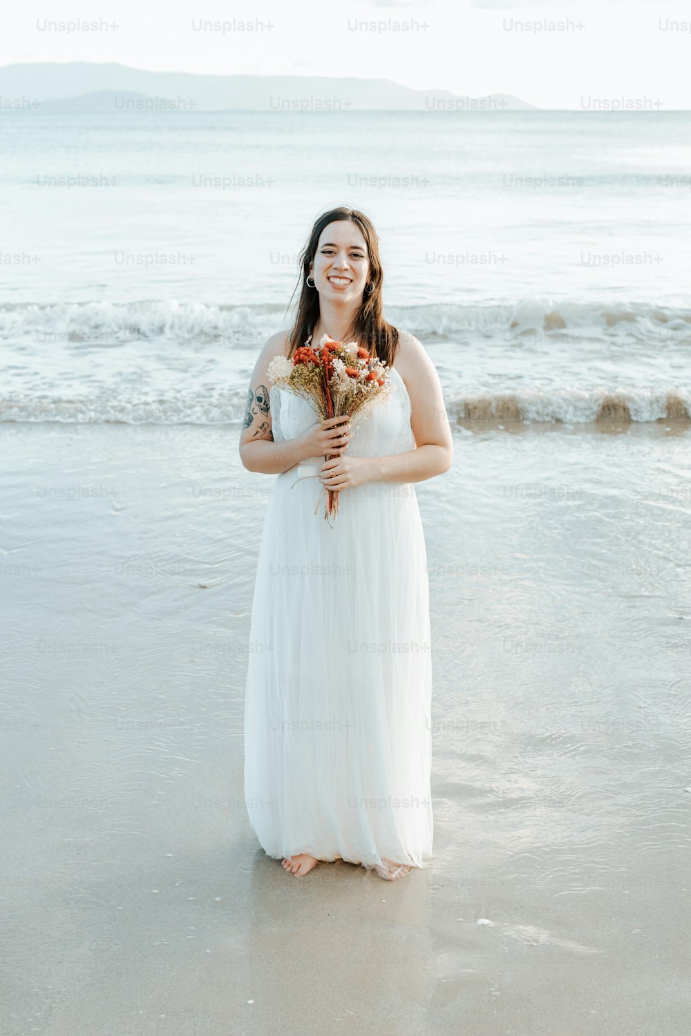 a woman standing on a beach holding a bouquet of flowers