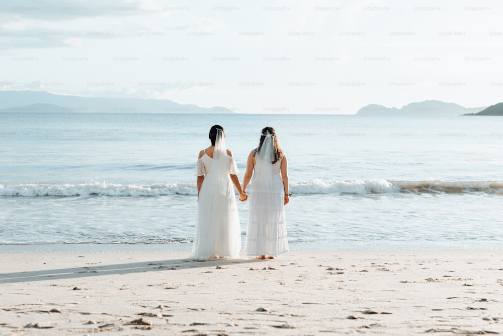 um casal de mulheres em pé no topo de uma praia de areia