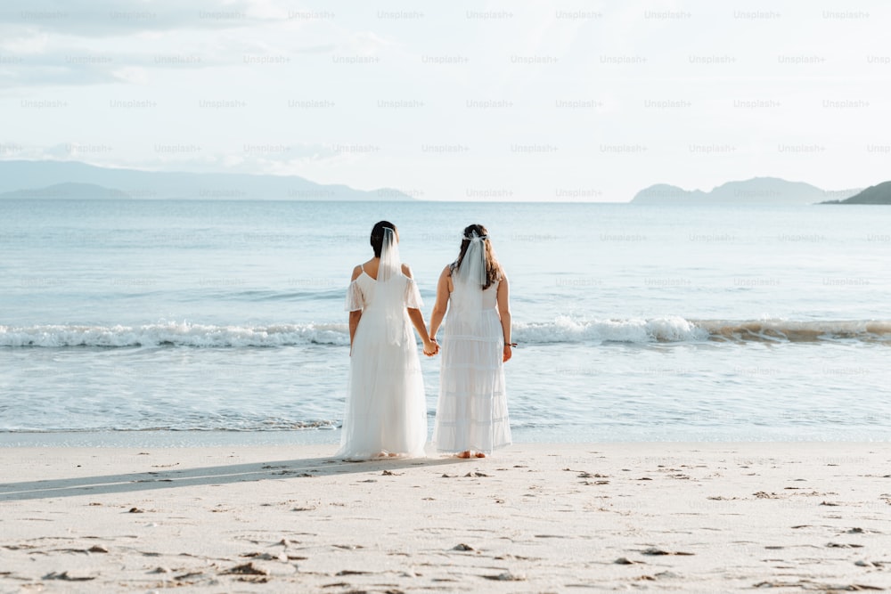 Un par de mujeres de pie en la cima de una playa de arena