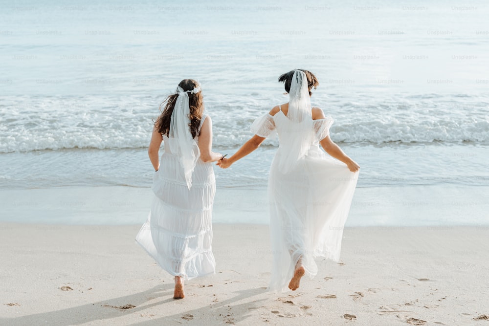 Zwei Bräute gehen am Strand spazieren und halten sich an den Händen