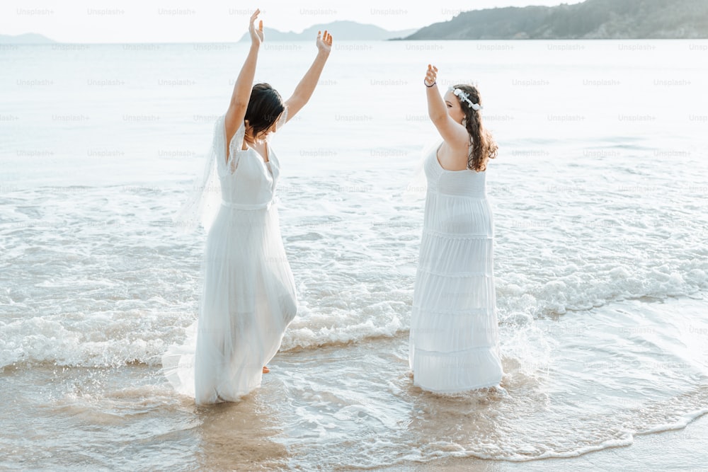 two women in white dresses are standing in the water