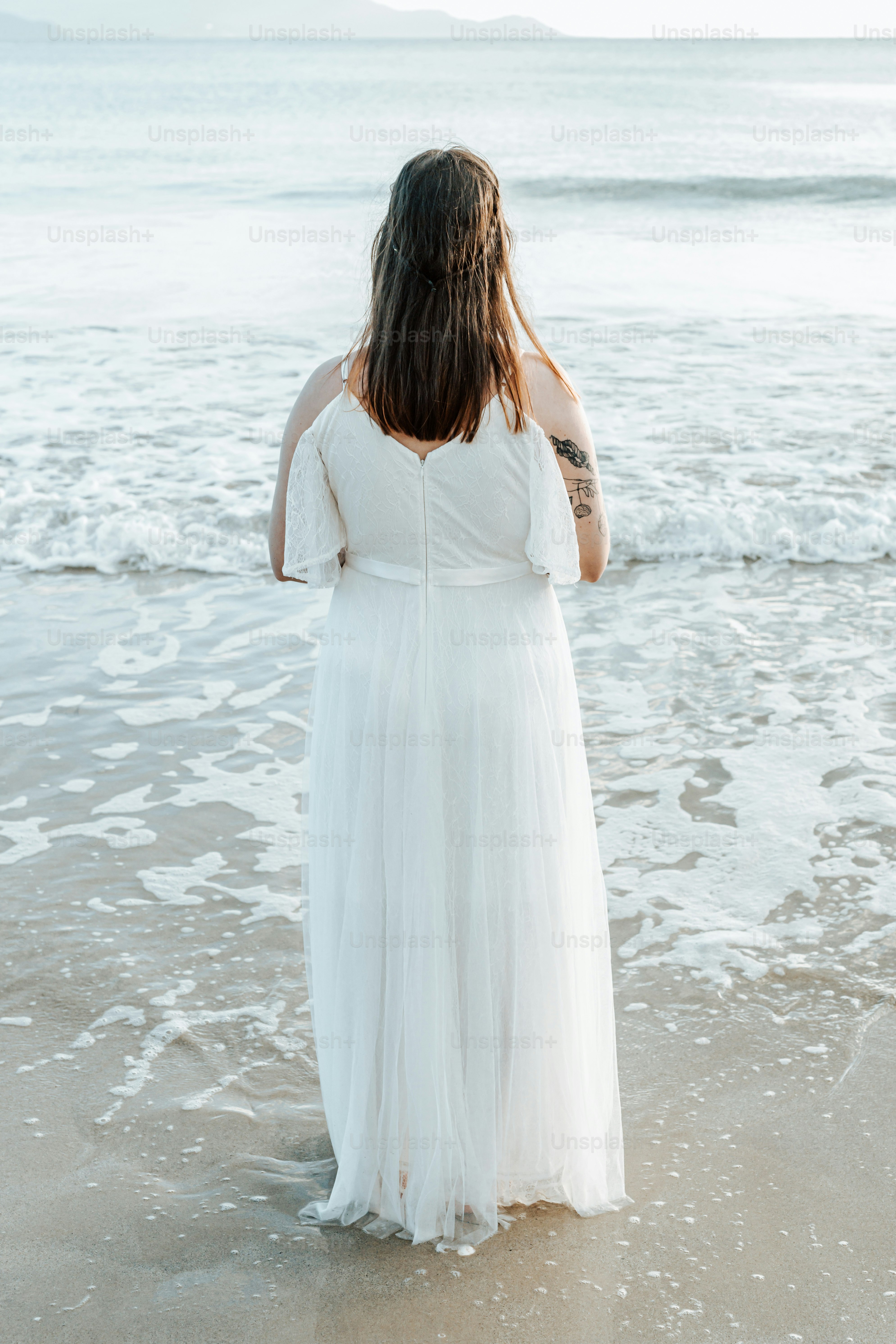 a woman in a white dress standing on a beach