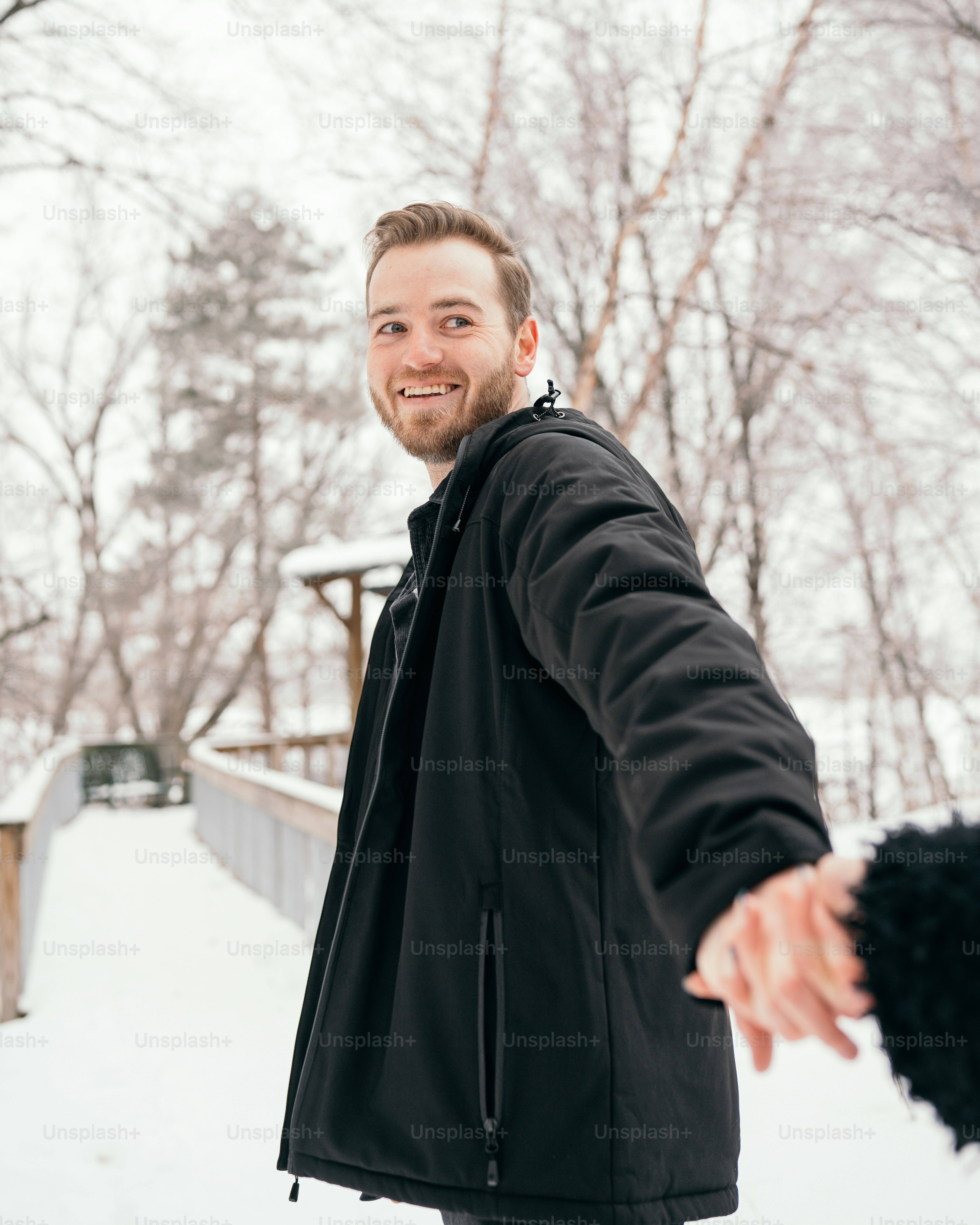a man in a black jacket holding his hand out in the snow
