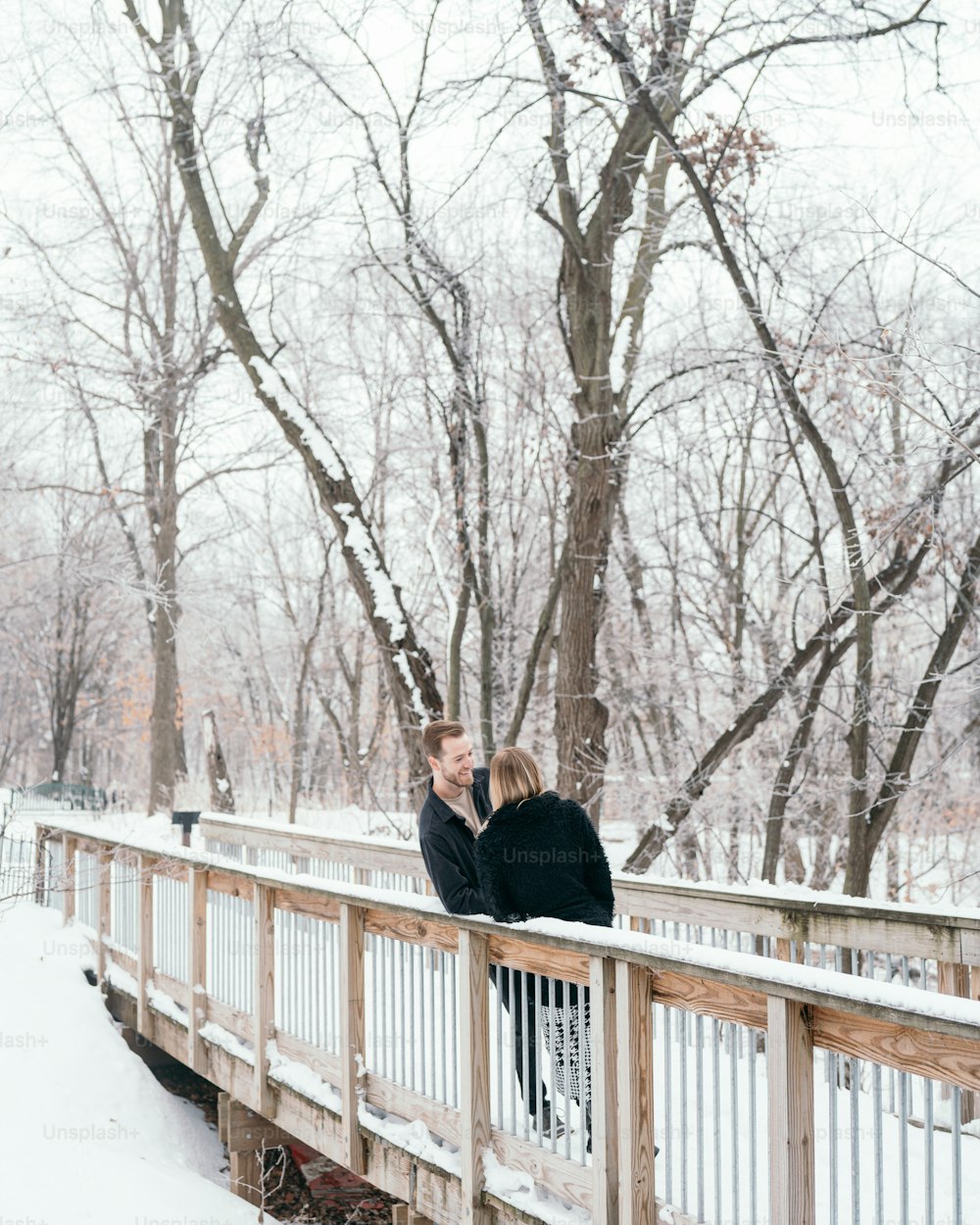 duas pessoas de pé em uma ponte na neve