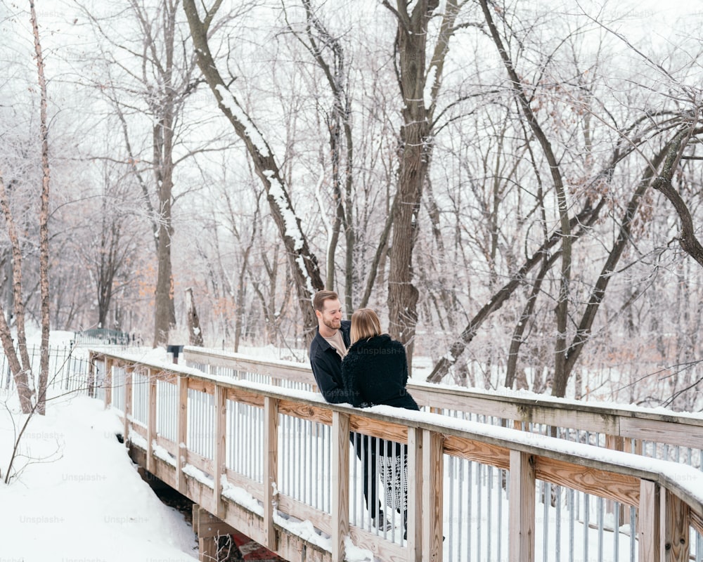 a man and woman standing on a bridge in the snow