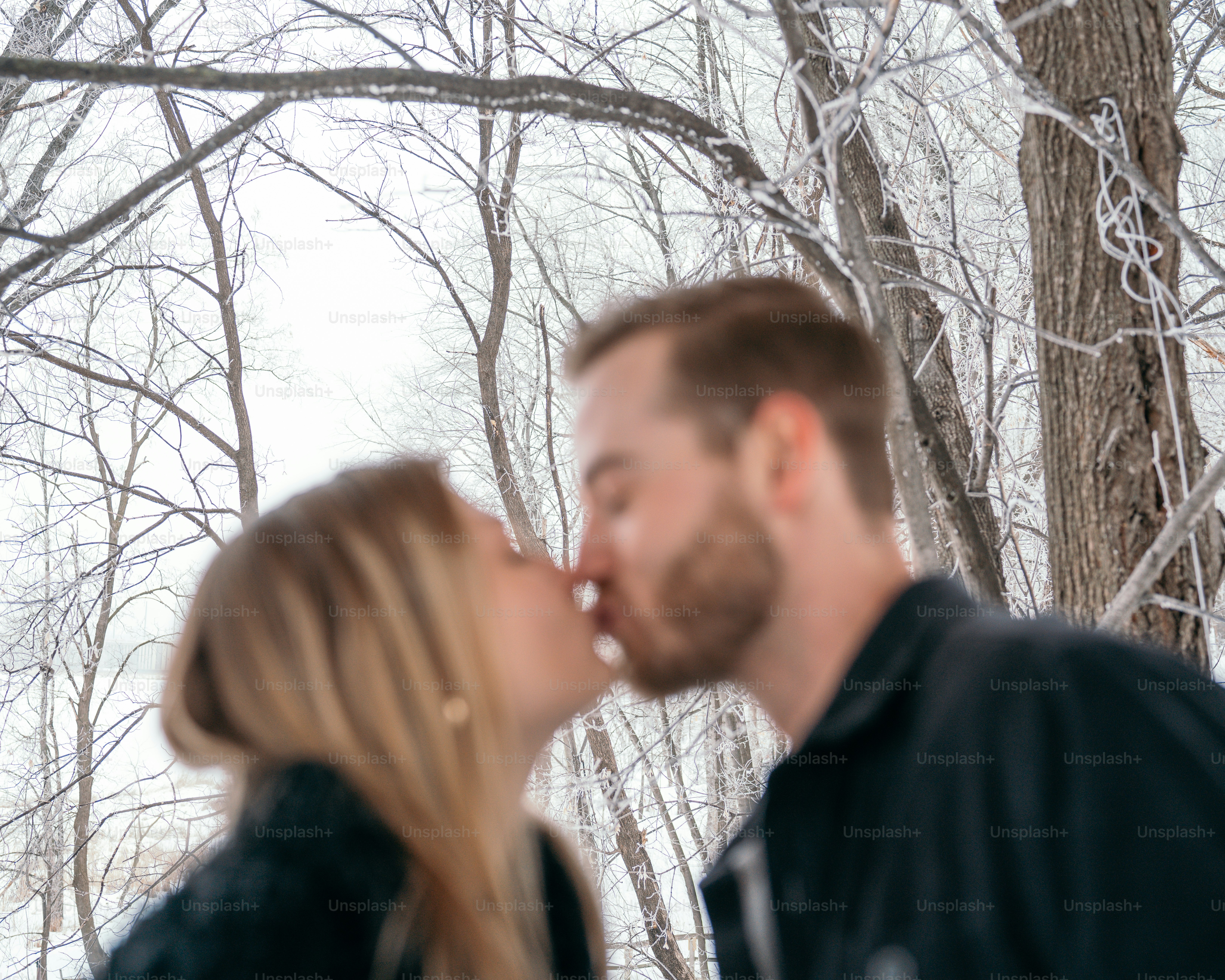 a man and a woman kissing in front of a tree