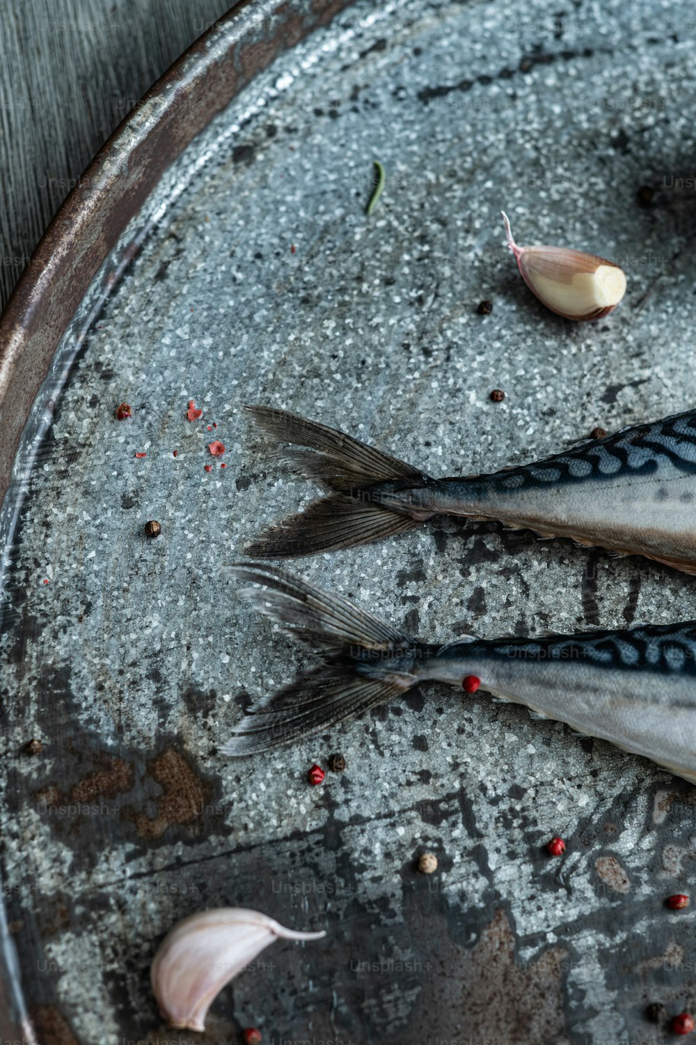 two dead fish on a metal tray with garlic and garlic