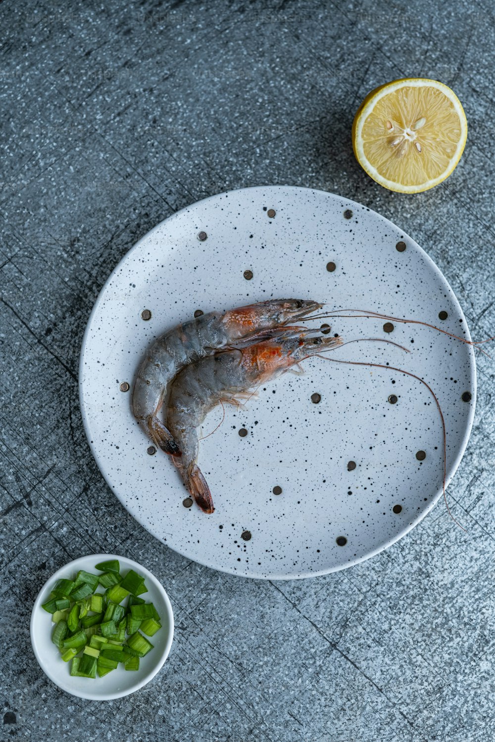 um prato branco coberto com um camarão cozido ao lado de uma tigela de cebolas verdes picadas