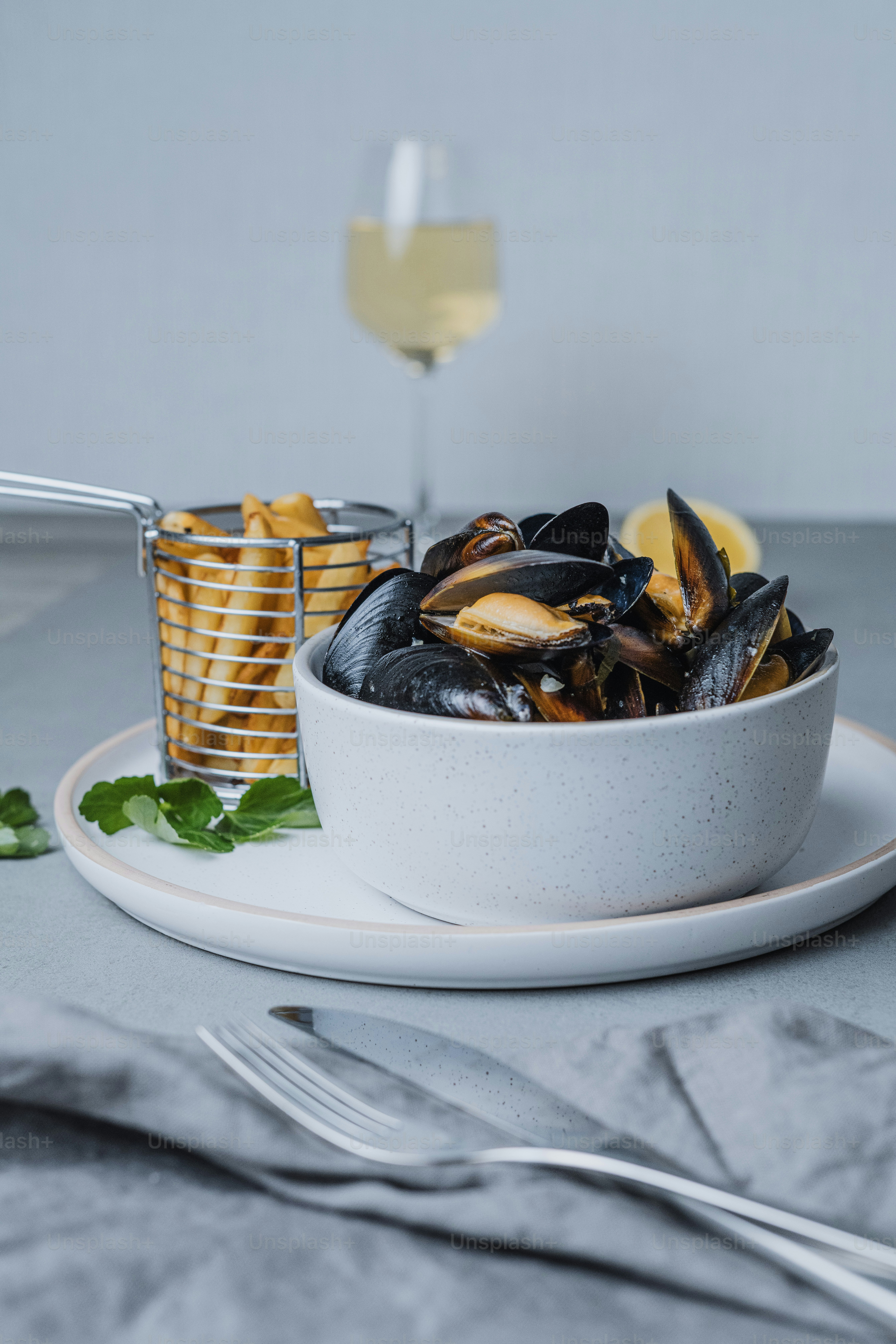 a white bowl filled with mussels next to a glass of wine